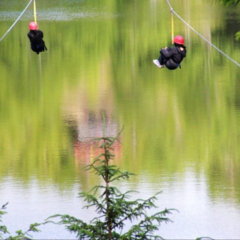 Two people zipline over a lake in Warrenton