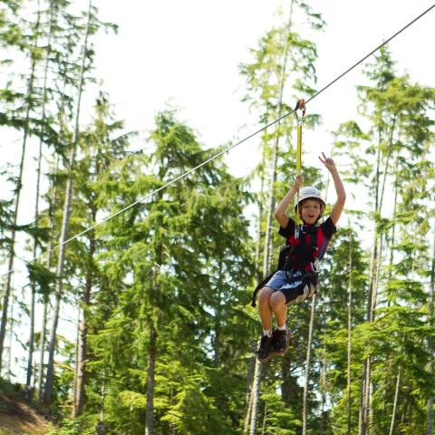 A boy gives the peace sign as he zip lines