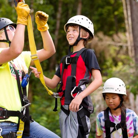 A guide helps a boy zip-line with High Life Adventures