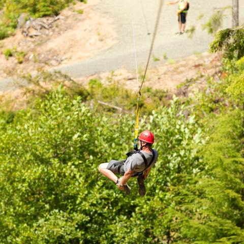 A man grabs his feet as he zip-lines