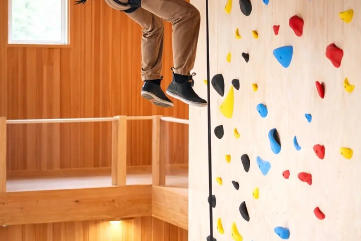 Person climbing indoor wall with colorful holds and safety harness.