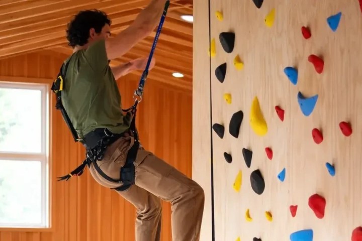 Person climbing indoor rock wall with colorful holds in wooden room.